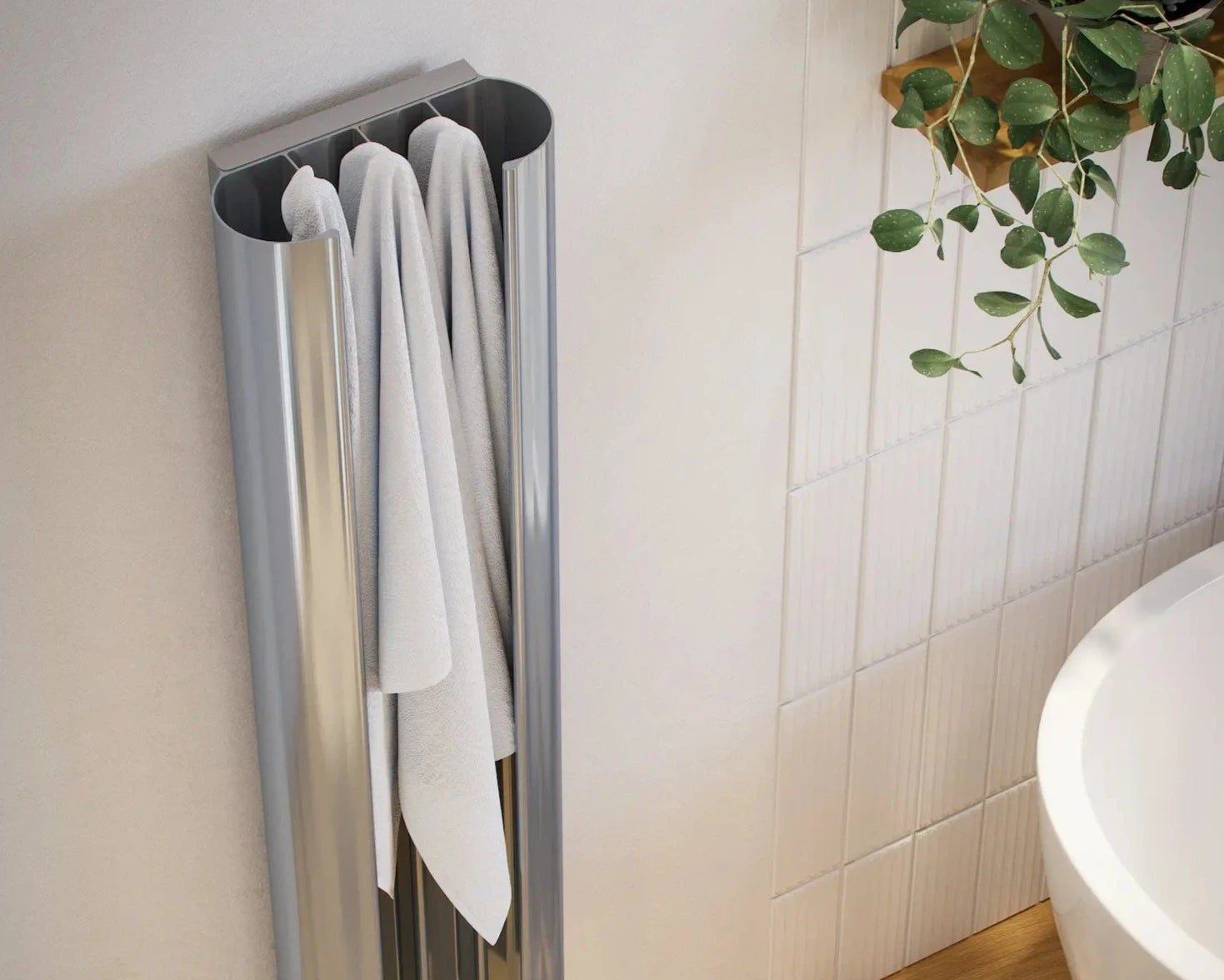 A silver heated towel rail mounted on a white wall with two towels hanging on it. The towels are white and appear to be made of a soft, absorbent material.
