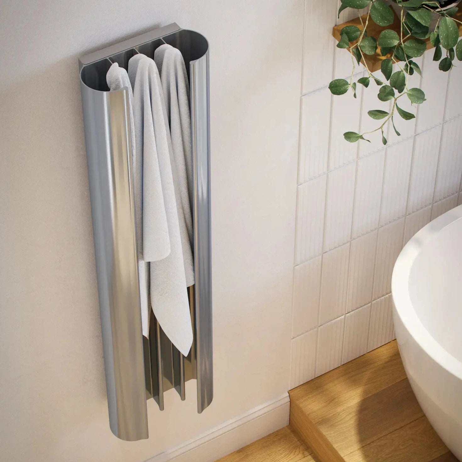 A silver heated towel rail mounted on a white wall with two towels hanging on it. The towels are white and appear to be made of a soft, absorbent material.